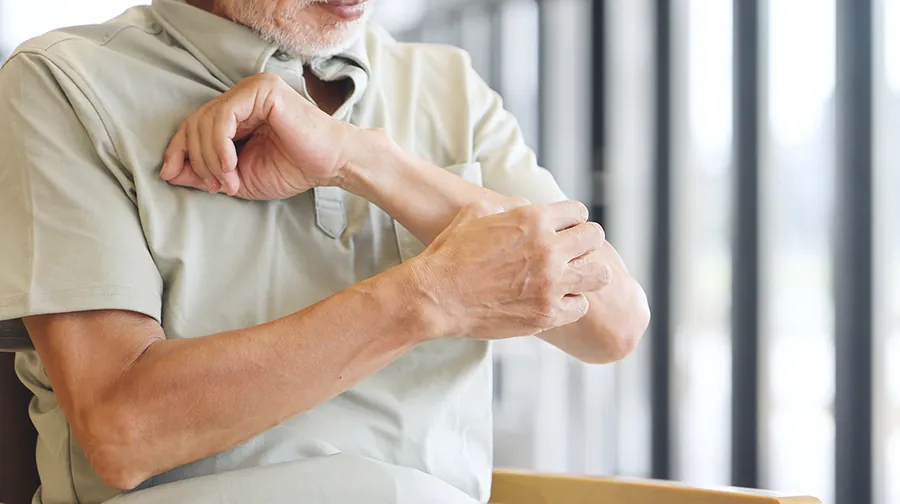 Älterer Mann kratzt sich am Arm